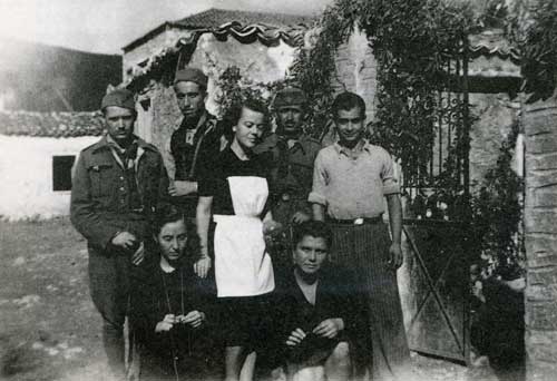 Με την λευκή ποδιά η συγγραφ�ας στην είσοδο του Πατρικού της σπιτιού στα Δίδυμα περίπου το 1943. Φωτογραφία από το βιβλίο, Γιόνα Μικ� Παϊδούση, « Ο Κόκκινος Επιτάφιος », Εκδόσεις Βιβλιόραμα, Αθήνα 2008.     