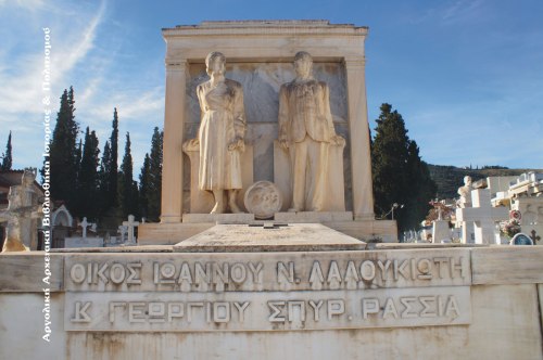 Νεκροταφείο Παναγίας, τάφος οικογένειας Ιωάννου Ν. Λαλουκιώτη (+1951). Πάνω σε κιβωτιόσχημη βάση, που καλύπτει τον τάφο, και μπρος σε κατασκευή που μιμείται κλασσική πρόσοψη οικίας (πεσσοί, επιστύλιο) τα ολόσωμα αγάλματα των Αρτεμισίας I. Λαλουκιώτη (1887-1942) και Ιωάννου Ν. Λαλουκιώτη (1882-1951). Ανάμεσα στα δυο αγάλματα κυκλική πλάκα με τις μορφές κατά κρόταφο και σε ελαφρό ανάγλυφο γέροντα με φέσι και γερόντισσας με τσεμπέρι. Υπογραφή: «Ε. ΤΖΩΡΤΖΑΚΗΣ ΕΠΙΟΙΕΙ». (Κώστα Δανούση, Έργα τηνιακών έντεχνων και λαϊκών γλυπτών στα νεκροταφεία της Ελλάδας, Αθήνα 1988). Φωτογραφία: Ηλίας Αντωνάκος, 2015. 